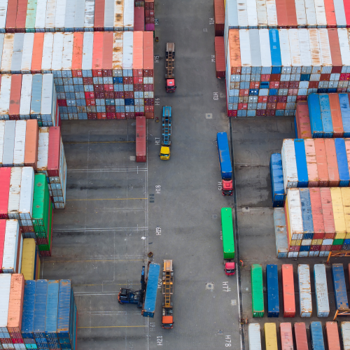 Logistics Image of shipping containers, semis, and a crane at a shipping yard